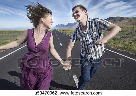 Stock Image - Mid adult couple running on road holding hands, Lanzarote, Spain. Fotosearch