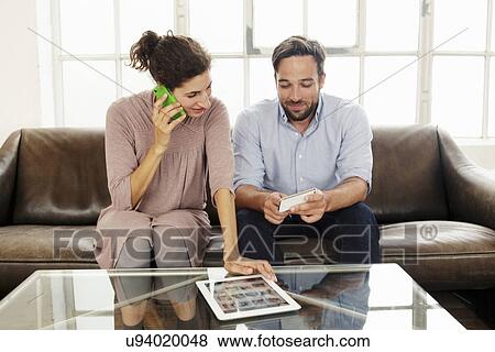 Stock Photo - Mid adult couple with digital tablet, woman on cell phone. Fotosearch