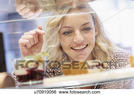 Stock Photograph - Mid adult female choosing from cake display in cafe. Fotosearch