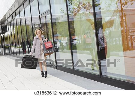 Stock Image - Mid adult female shopper walking on street with bags. Fotosearch