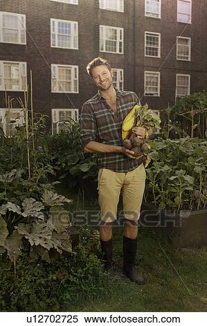 Stock Photography - Mid adult man with harvested beetroot on council estate allotment. Fotosearch