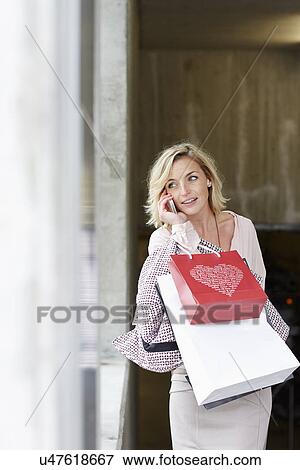 Stock Photo - Mid adult woman shopper using mobile phone. Fotosearch