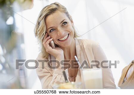 Mid adult woman talking on mobile phone in cafe View Large Photo Image Stock Photo - Mid adult woman talking on mobile phone in cafe. Fotosearch