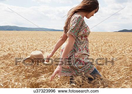 Stock Photograph - Mid adult woman walking through wheat field. Fotosearch