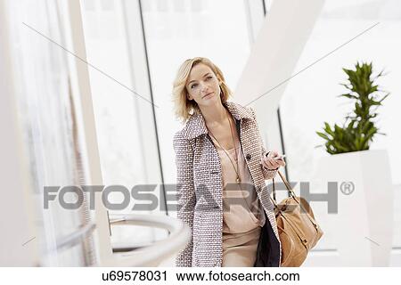 Stock Image - Mid adult woman with trolley case arriving at city airport. Fotosearch