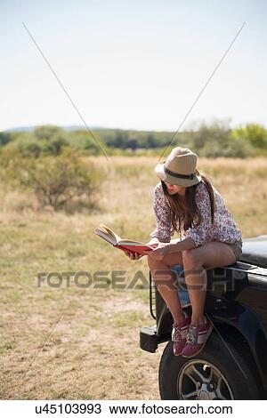 Mid adult women sitting on hood of car reading book View Large Photo Image Stock Image - Mid adult women sitting on hood of car reading book. Fotosearch