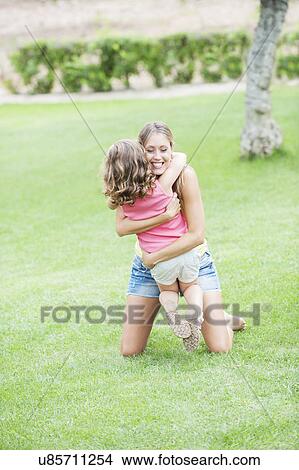 Picture - Mother and daughter hugging on lawn. Fotosearch