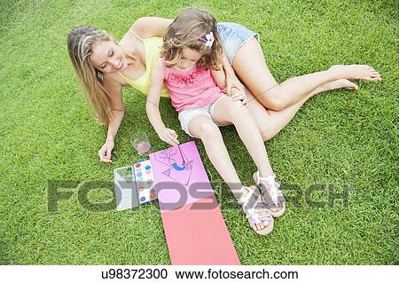 Stock Image - Mother and daughter painting, sitting on grass. Fotosearch