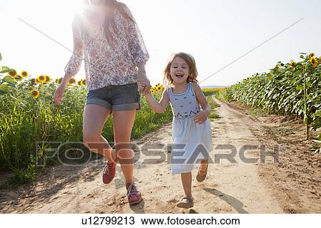 Stock Image - Mother and daughter running through field of sunflowers. Fotosearch