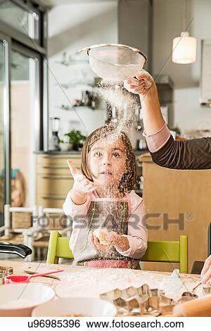 Stock Photograph - Mother and daughter sieving flour in kitchen. Fotosearch