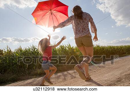 Mother and daughter walking through field carrying red umbrella View Large Photo Image Stock Photo - Mother and daughter walking through field carrying red umbrella. Fotosearch