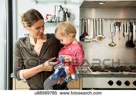 Stock Photography - Mother carrying baby girl in kitchen. Fotosearch