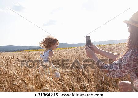 Stock Photography - Mother photographing girl running through wheat field. Fotosearch