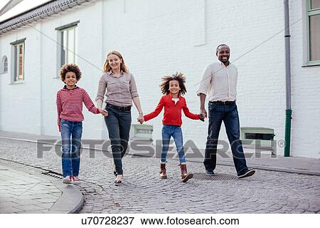 Stock Photo - Parents and two children walking and holding hands on street. Fotosearch