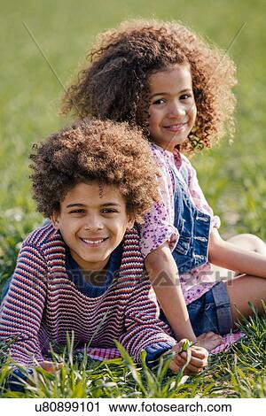 Stock Image - Portrait of brother and sister lying on grass in sunlight. Fotosearch