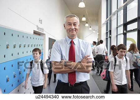 Stock Image - Portrait of male teacher with arms folded in school corridor. Fotosearch