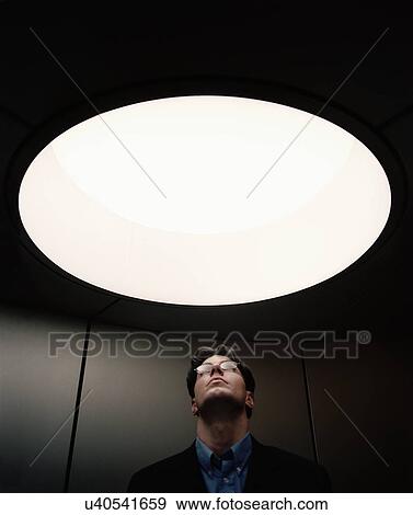 Stock Photo - Portrait of mid adult male staring through circular ceiling window. Fotosearch