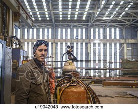 Stock Photo - Portrait of welder wearing overalls and safety goggles in factory. Fotosearch