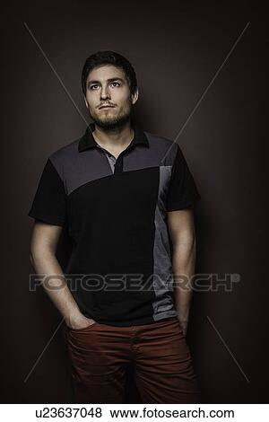 Stock Photo - Portrait of young man wearing t shirt with hands in pockets. Fotosearch