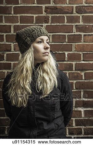 Portrait of young woman by brick wall wearing knit hat View Large Photo Image Stock Photography - Portrait of young woman by brick wall wearing knit hat. Fotosearch