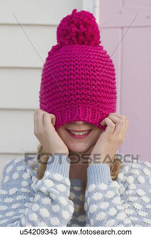 Stock Image - Portrait of young woman hiding under wooly hat. Fotosearch