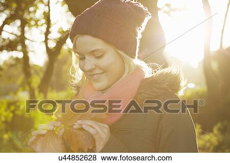 Portrait of young woman in park, holding autumn leaf View Large Photo Image Stock Photo - Portrait of young woman in park, holding autumn leaf. Fotosearch