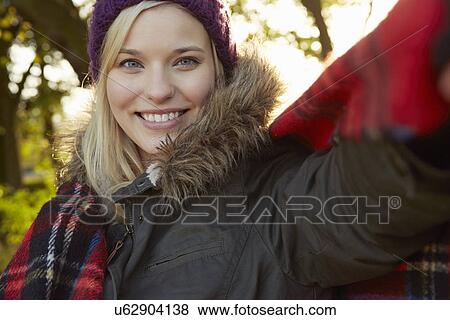 Stock Photo - Portrait of young woman in park, tartan picnic blanket around shoulders. Fotosearch