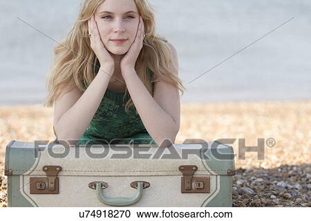 Stock Image - Portrait of young woman with suitcase on beach, Whitstable, Kent, UK. Fotosearch