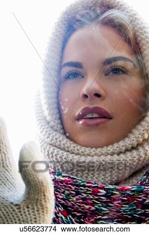 Picture - Portrait of young woman wrapped up looking through window. Fotosearch