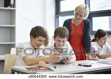 Stock Image - Schoolchildren working in class with teacher. Fotosearch
