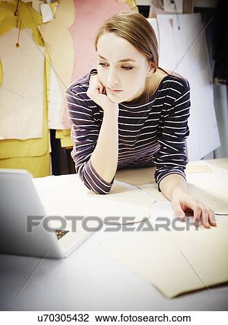 Stock Image - Seamstress working at table. Fotosearch