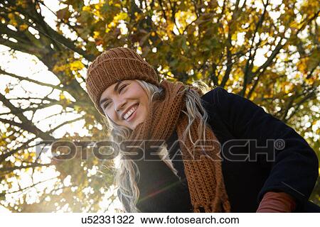 Stock Image - Smiling young woman wrapped up in autumnal park. Fotosearch