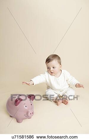 Stock Photograph - Studio portrait of baby girl reaching for piggy bank. Fotosearch