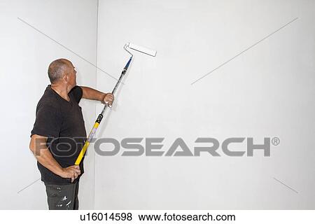 Stock Photo - Studio shot of senior roller painting room walls. Fotosearch