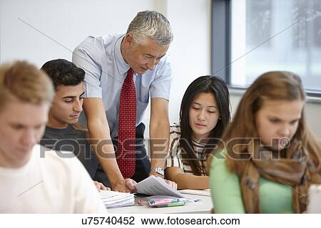 Stock Image - Teacher working with teenagers in classroom. Fotosearch