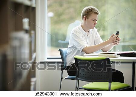 Teenage boy using cell phone in library View Large Photo Image Stock Image - Teenage boy using cell phone in library. Fotosearch