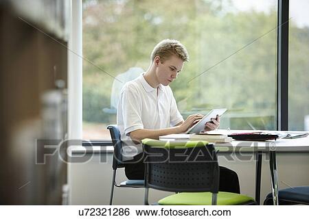 Stock Photograph - Teenage boy using digital tablet in library. Fotosearch