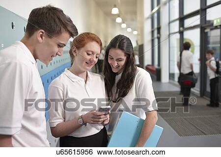 Teenagers looking at mobile phone in school corridor View Large Photo Image Stock Photograph - Teenagers looking at mobile phone in school corridor. Fotosearch
