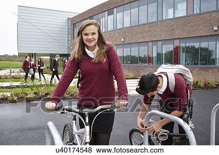 Stock Photo - Teenagers unlocking cycles outside school. Fotosearch