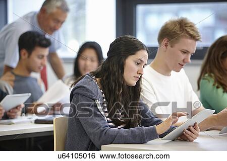 Stock Photograph - Teenagers working with digital tablets classroom. Fotosearch