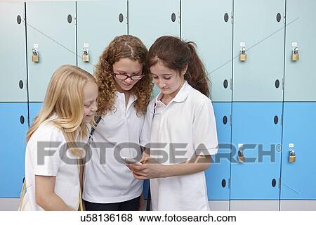 Stock Photo - Three female school friends looking at mobile phone. Fotosearch