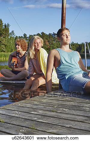 Stock Image - Three young adult friends relaxing on pier, Gavle, Sweden. Fotosearch