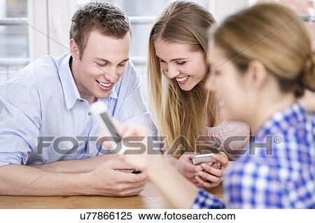 Three young people looking at cell phones and smiling View Large Photo Image Stock Photography - Three young people looking at cell phones and smiling. Fotosearch