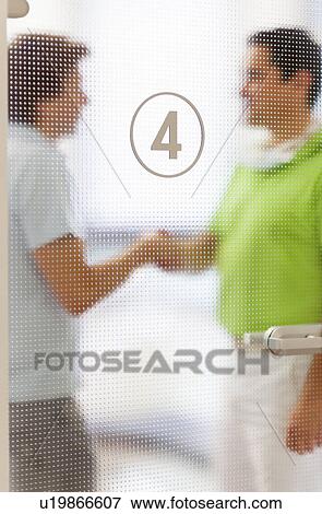 Two men shaking hands behind glass door View Large Photo Image Stock Photo - Two men shaking hands behind glass door. Fotosearch