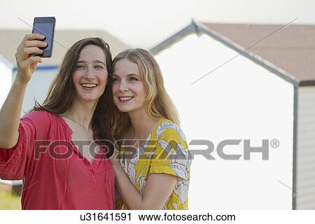 Stock Image - Two young female friends taking self portrait, Whitstable, Kent, UK. Fotosearch