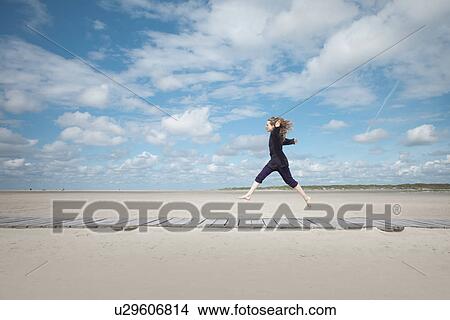 Picture - Woman jumping on boardwalk, Sankt Peter Ordings, Schleswig Holstein, Germany. Fotosearch