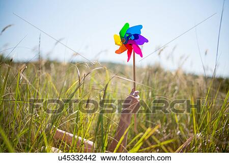 Stock Image - Woman lying in long grass holding windmill. Fotosearch