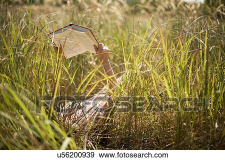 Woman lying in long grass reading book View Large Photo Image Stock Photo - Woman lying in long grass reading book. Fotosearch