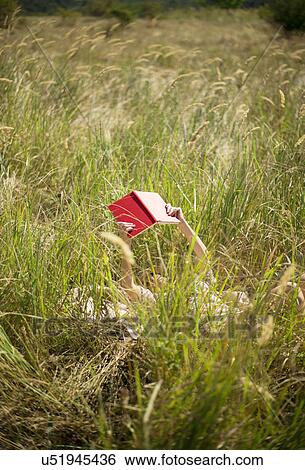 Stock Photograph - Woman lying in long grass reading book. Fotosearch