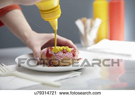 Stock Image - Woman squirting donut with ketchup and mustard. Fotosearch